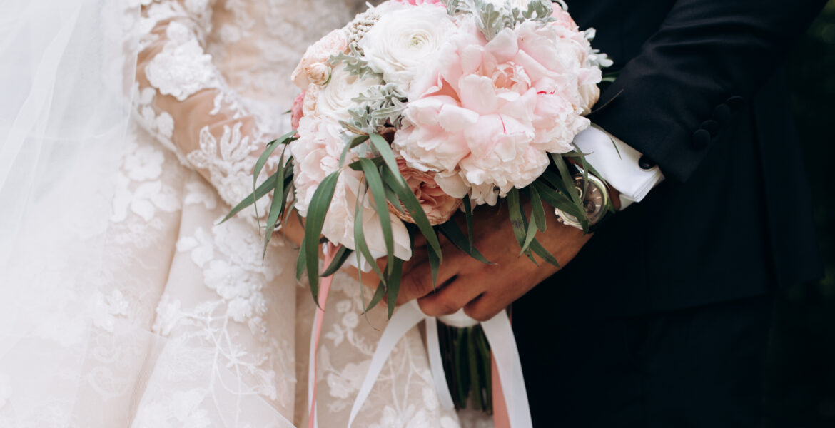 Frontview of groom and brides hands together are holding wedding pink bouquet